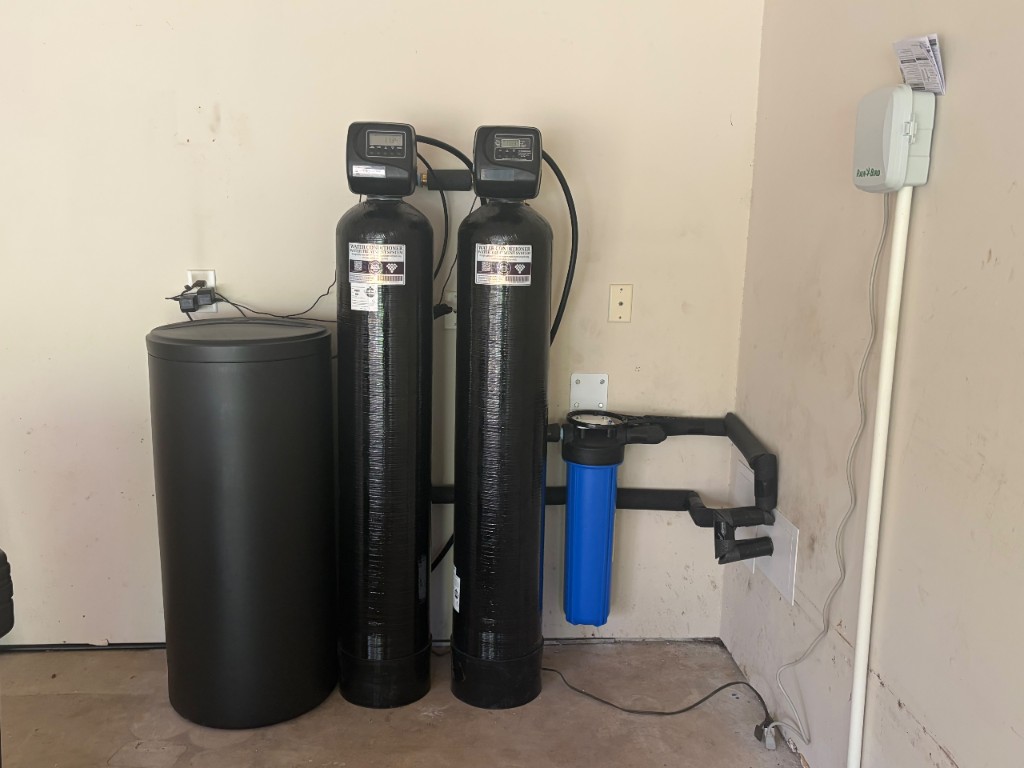 Twin-tank water softener with brine tank and pre-filter installed in a garage corner