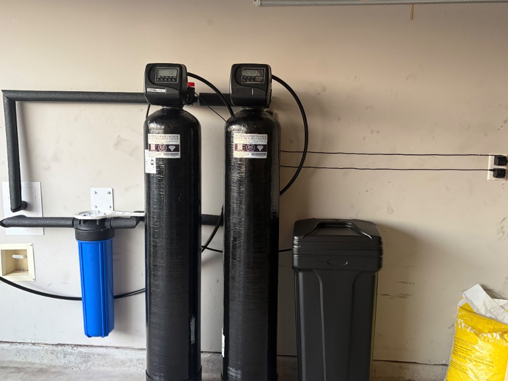 Pre-filter, water softener, catalytic carbon tank and brine tank installed side by side in a garage